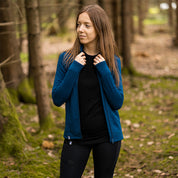 Frau im Wald trägt Merino Jacke Damen 270 g/m², ideal für Outdoor-Abenteuer, bietet Komfort und Funktionalität durch hochwertige Merinowolle.