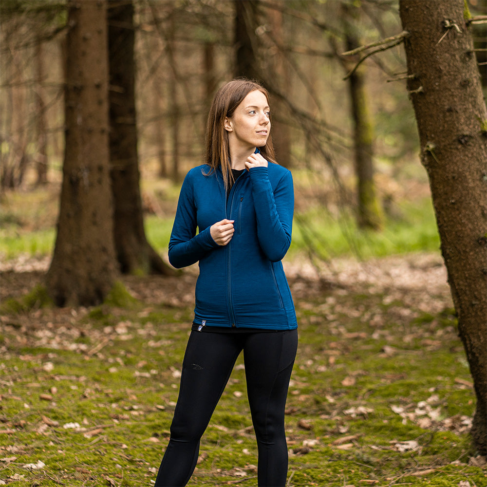 Frau im Wald trägt die Merino Jacke Damen 270 g/m2 von Alpin Loacker, ideal für Outdoor-Abenteuer und flexiblen Komfort.