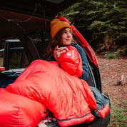 Frau sitzt im Auto mit dem Down Pro 3 Jahreszeiten Schlafsack 860g, ideal für Trekking und Camping bei kühlen Temperaturen.