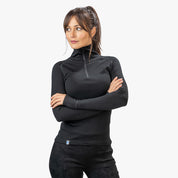 Merino Langarmshirt mit Zip Damen 230g/m², Frau mit verschränkten Armen, betont Vielseitigkeit und Komfort, ideal für Outdoor-Aktivitäten und Reisen.