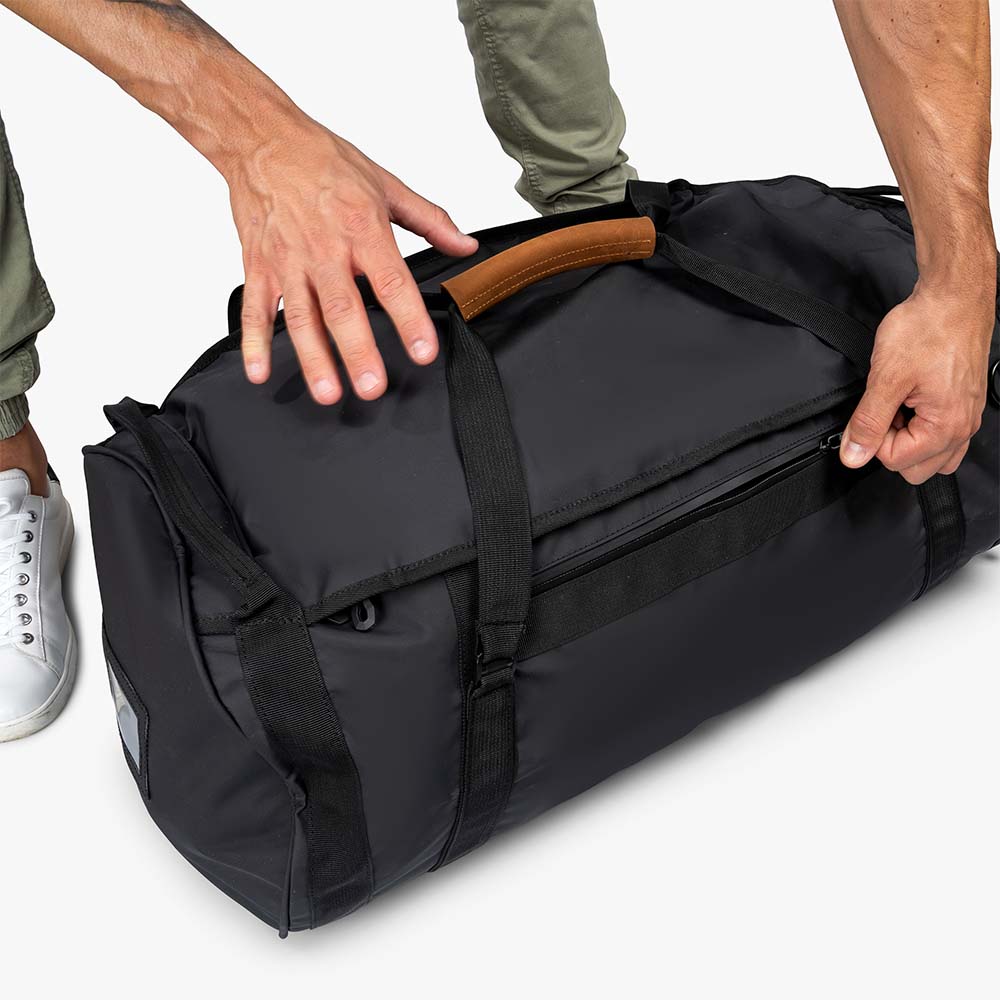 Person hält Alpin Loacker Reisetasche, Sporttasche & Duffel Bag mit Ledergriff. Perfekt für Reisen, wasser- und schmutzabweisend, wandelbar zum Rucksack.