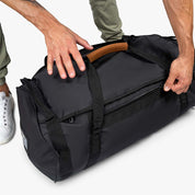 Person hält Alpin Loacker Reisetasche, Sporttasche & Duffel Bag mit Ledergriff. Perfekt für Reisen, wasser- und schmutzabweisend, wandelbar zum Rucksack.