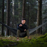 Hombre sentado en el bosque en una hamaca exterior negra y gris Alpin Loacker 