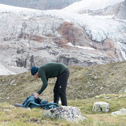 Mann mit Softshell Wanderhose Herren steht in grasiger Landschaft, trägt Rucksack. Perfekte Wahl für Outdoor-Abenteuer, bietet Komfort und Flexibilität.