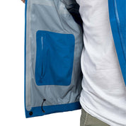 Person trägt Herren 3 Lagen Hardshell Regenjacke, leicht und funktional für Outdoor-Aktivitäten; zeigt Detailansicht der strapazierfähigen, wasserdichten und atmungsaktiven blauen Jacke.