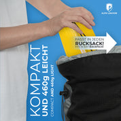 Person legt gelbe Tasche in schwarze Tasche, zeigt die Ultraleichte Isomatte isoliert mit Kunstdaune - 460g, ideal für Outdoor-Abenteuer und minimalen Platzbedarf.