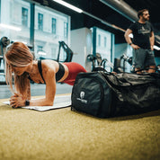 Reisetasche, Sporttasche & Duffel Bag auf dem Boden im Fitnessstudio, ideal für Abenteuer, mit wasserabweisendem Material und vielseitigen Trageoptionen.