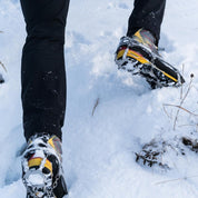 Person trägt Alpin Loacker Chain Pro 18 Grödeln auf schneebedecktem Weg, zeigt Schuh mit Spikes und Ketten für sicheren Halt auf rutschigen Winterpfaden.