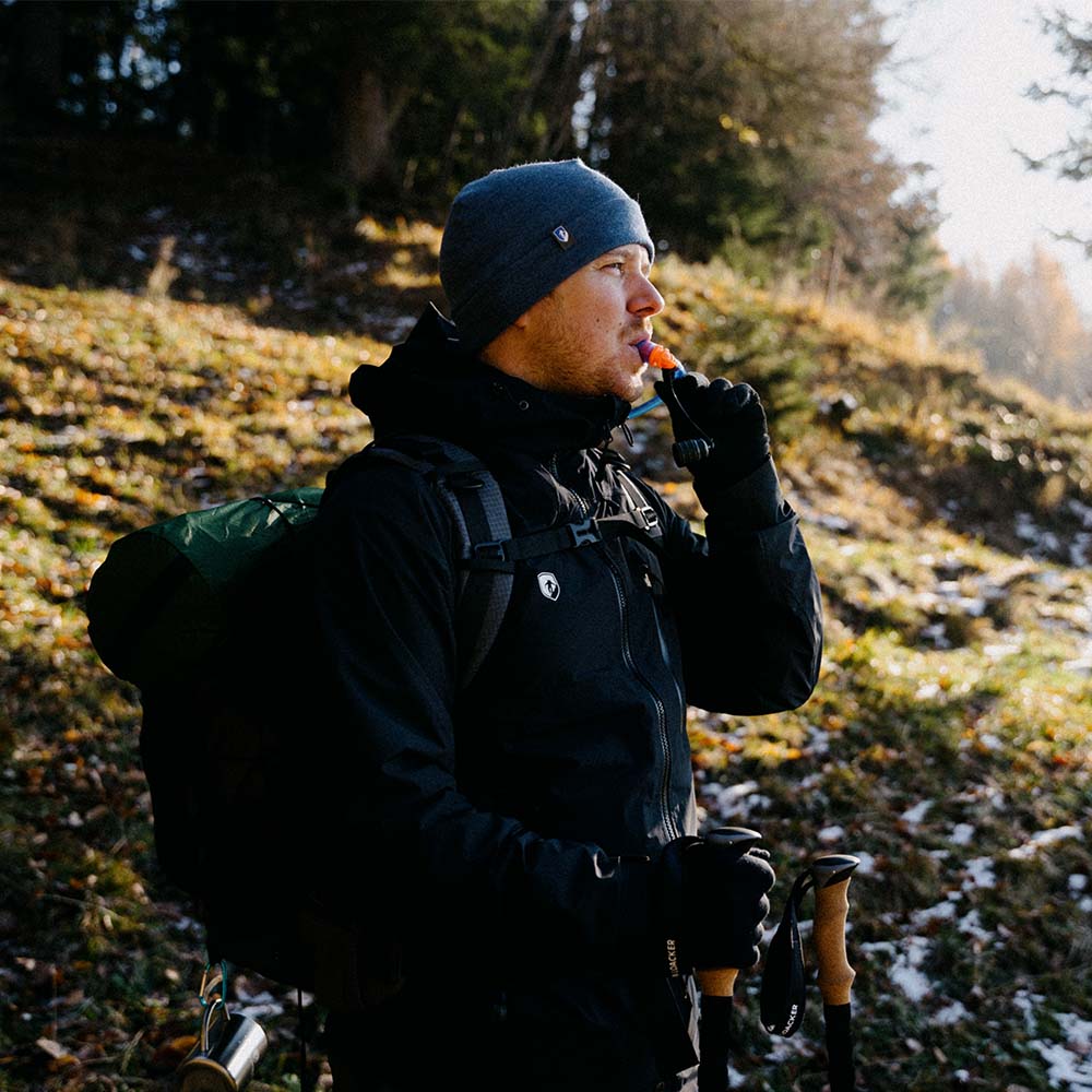 Mann mit Ultraleichter Wanderrucksack 40+5 Liter, beim Wandern mit Pfeife und Wanderstock. Ideal für mehrtägige Outdoor-Abenteuer, robust und leicht.